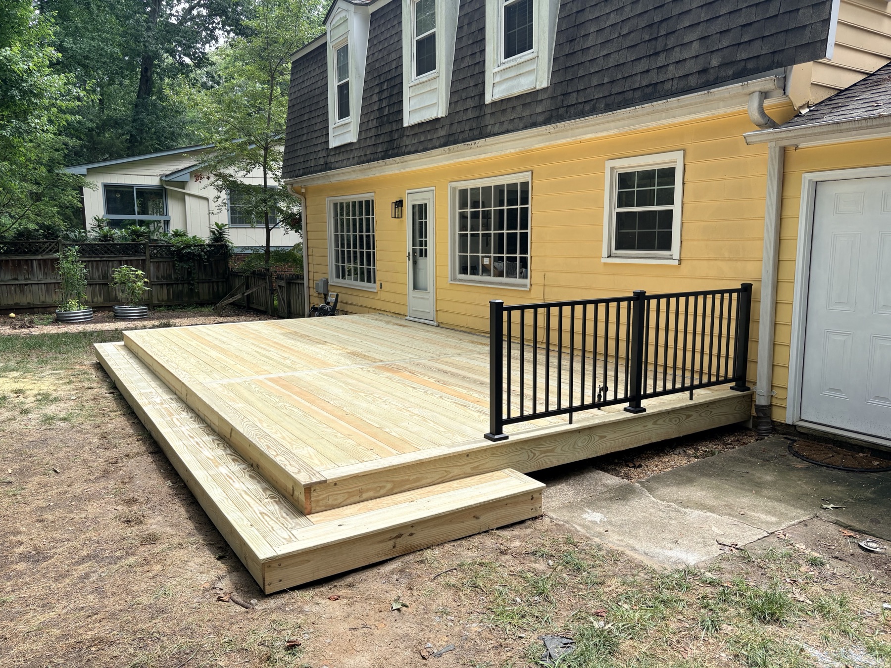 A ground-level wood deck with a black metal railing, wrapped tight to the corner of the house.